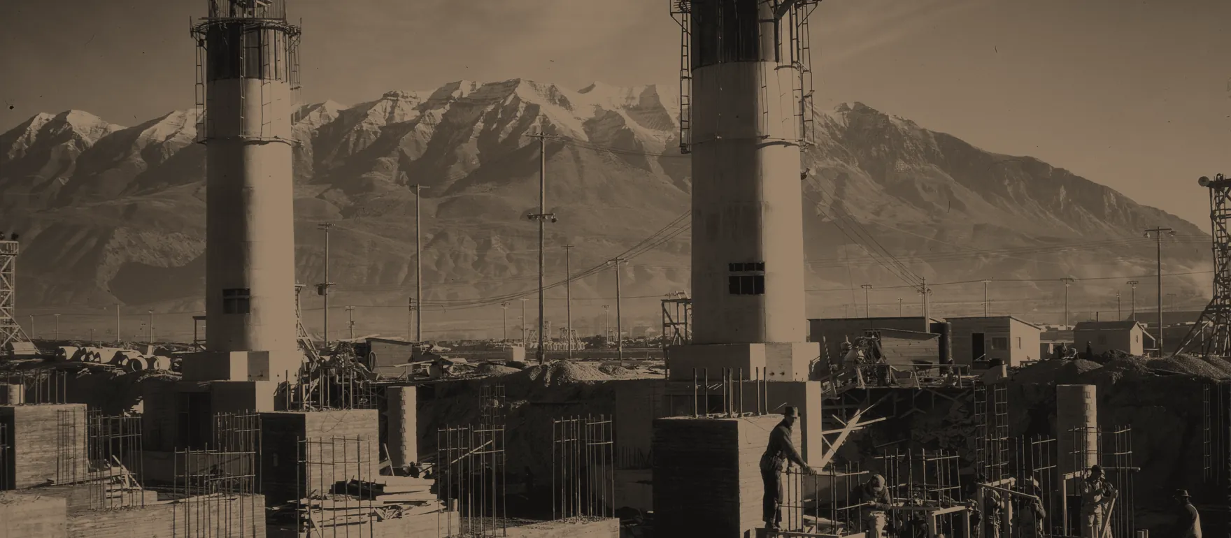 Steel works under construction in 1942, with workers on the foundations and snow-capped mountains behind