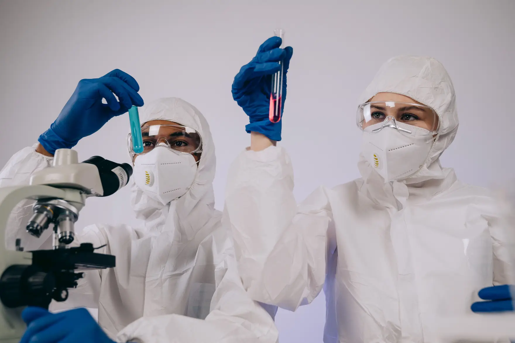 Two researchers in coveralls, goggles, respirators and gloves holding up test tubes