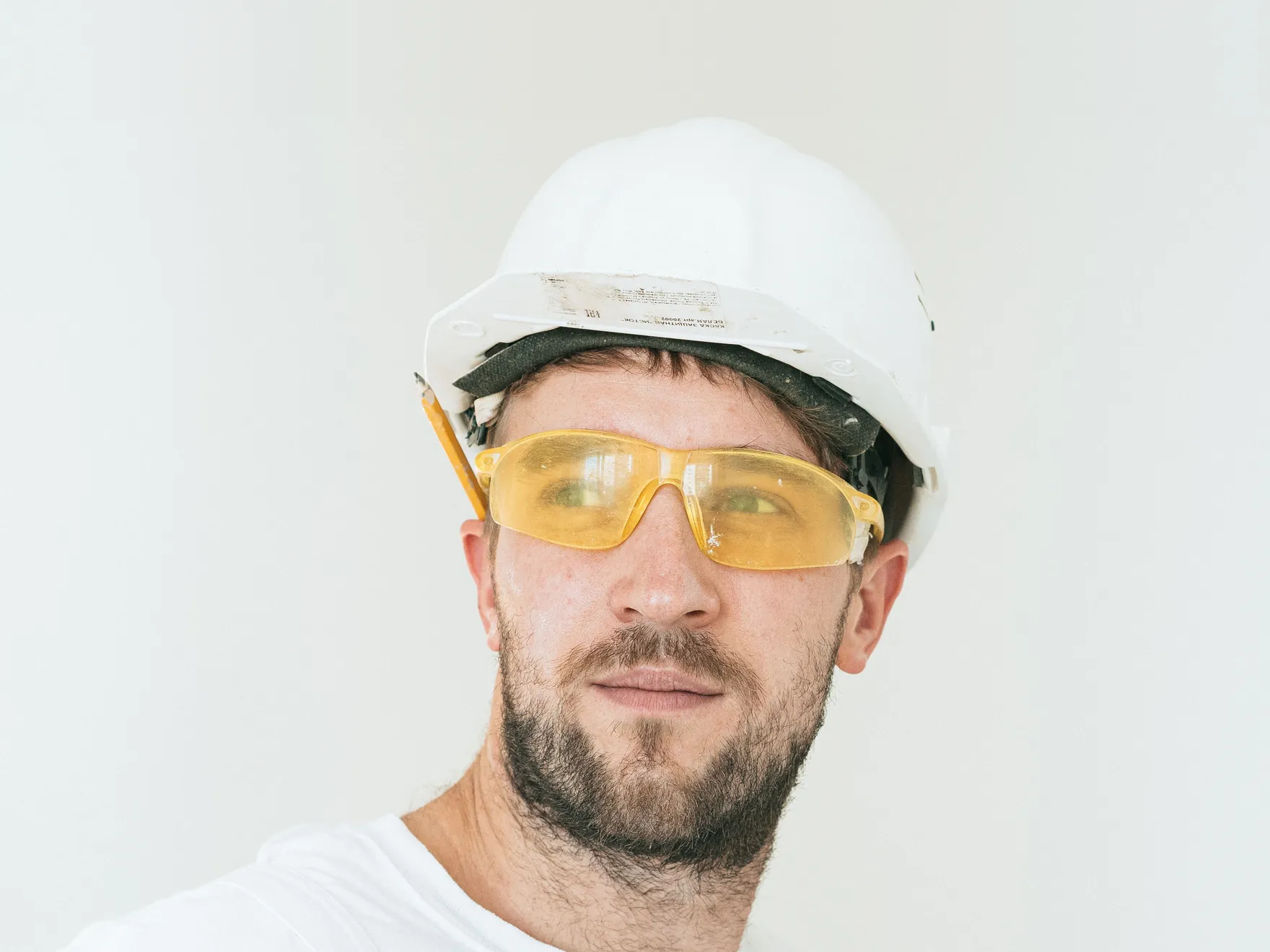 A bearded man in a white hard hat and yellow safety glasses