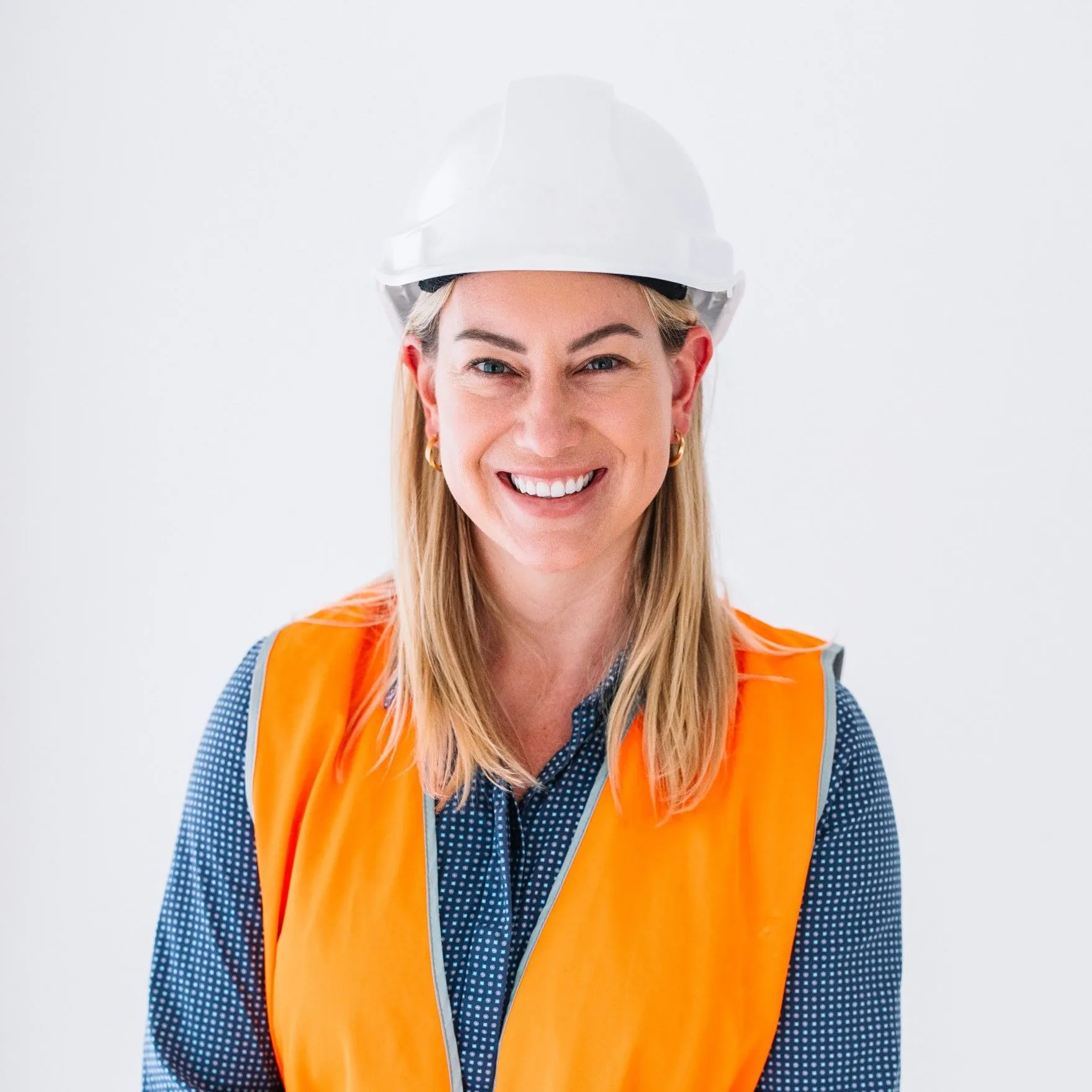 A smiling woman in a white hard hat and an orange high-visibility vest